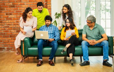 Hintli Asyalı genç girişimci, modern bir ofiste dizüstü bilgisayar ve belgelerle birlikte bir kanepede otururken fikir üretme ya da gayri resmi bir toplantıda strateji planlama ekibi kuruyor.