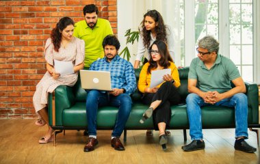 Hintli Asyalı genç girişimci, modern bir ofiste dizüstü bilgisayar ve belgelerle birlikte bir kanepede otururken fikir üretme ya da gayri resmi bir toplantıda strateji planlama ekibi kuruyor.