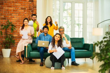 Hintli Asyalı genç girişimci, modern bir ofiste dizüstü bilgisayar ve belgelerle birlikte kanepede otururken gayri resmi bir toplantıda strateji planlarken başarıyı kutluyor.