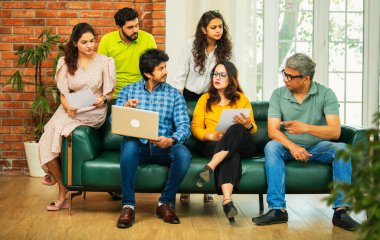 Hintli Asyalı genç girişimci, modern bir ofiste dizüstü bilgisayar ve belgelerle birlikte bir kanepede otururken fikir üretme ya da gayri resmi bir toplantıda strateji planlama ekibi kuruyor.