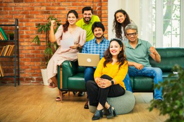 Hintli Asyalı genç girişimci, modern bir ofiste dizüstü bilgisayar ve belgelerle birlikte kanepede otururken gayri resmi bir toplantıda strateji planlarken başarıyı kutluyor.