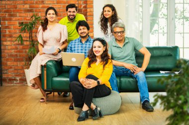 Hintli Asyalı genç girişimci, modern bir ofiste dizüstü bilgisayar ve belgelerle birlikte kanepede otururken gayri resmi bir toplantıda strateji planlarken başarıyı kutluyor.