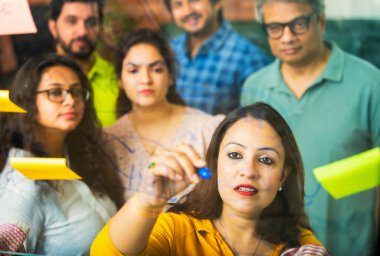 Hintli Asyalı genç iş adamları ya da yeni başlayan profesyonellerden oluşan bir grup. Fikir üreten, stratejileri tartışan, cam duvarın önünde kalem kullanarak projeler planlayan, modern ofisteki yapışkan notlar.