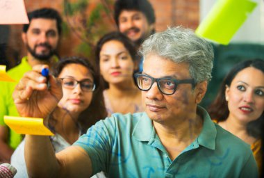 Hintli Asyalı genç iş adamları ya da yeni başlayan profesyonellerden oluşan bir grup. Fikir üreten, stratejileri tartışan, cam duvarın önünde kalem kullanarak projeler planlayan, modern ofisteki yapışkan notlar.