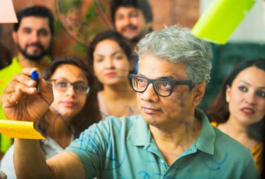 Hintli Asyalı genç iş adamları ya da yeni başlayan profesyonellerden oluşan bir grup. Fikir üreten, stratejileri tartışan, cam duvarın önünde kalem kullanarak projeler planlayan, modern ofisteki yapışkan notlar.