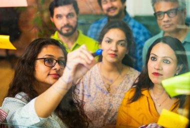 Hintli Asyalı genç iş adamları ya da yeni başlayan profesyonellerden oluşan bir grup. Fikir üreten, stratejileri tartışan, cam duvarın önünde kalem kullanarak projeler planlayan, modern ofisteki yapışkan notlar.