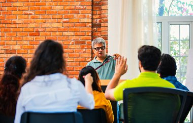Hintli Asyalı yaşam koçu, profesyonel akıl hocası konferansta bir grup genç girişimciye iş büyümesi girişimciliği hakkında ilham verici bir konuşma yapıyor, mikrofonla podyumda güvenle konuşuyor.