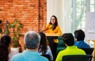 Hintli Asyalı yaşam koçu, profesyonel akıl hocası konferansta bir grup genç girişimciye iş büyümesi girişimciliği hakkında ilham verici bir konuşma yapıyor, mikrofonla podyumda güvenle konuşuyor.