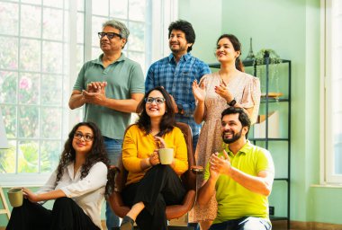 Modern girişim ofisindeki Hintli Asyalı genç şirket profesyonelleri, şık giyinmiş, el çırpıyor, başarıyı, başarıyı, takım çalışmasını, yeniliği, iş büyümesini kutluyorlar.