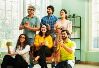 Modern girişim ofisindeki Hintli Asyalı genç şirket profesyonelleri, şık giyinmiş, el çırpıyor, başarıyı, başarıyı, takım çalışmasını, yeniliği, iş büyümesini kutluyorlar.