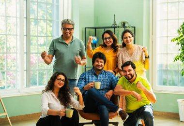 Modern girişim ofisindeki Hintli Asyalı genç şirket profesyonelleri, şık giyinmiş, el çırpıyor, başarıyı, başarıyı, takım çalışmasını, yeniliği, iş büyümesini kutluyorlar.