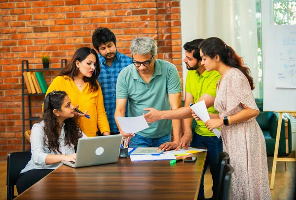 Hintli Asyalı genç iş adamları proje stratejisi üzerinde çalışan, belgeleri analiz eden, dizüstü bilgisayarda çalışan, iş geliştirme başarısı için samimi modern ofiste beyin fırtınası yapan bir ekip kurdular.