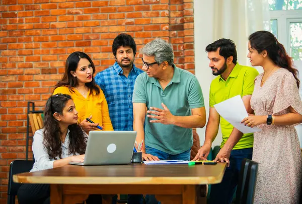 Hintli Asyalı genç iş adamları proje stratejisi üzerinde çalışan, belgeleri analiz eden, dizüstü bilgisayarda çalışan, iş geliştirme başarısı için samimi modern ofiste beyin fırtınası yapan bir ekip kurdular.