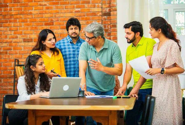 Hintli Asyalı genç iş adamları proje stratejisi üzerinde çalışan, belgeleri analiz eden, dizüstü bilgisayarda çalışan, iş geliştirme başarısı için samimi modern ofiste beyin fırtınası yapan bir ekip kurdular.