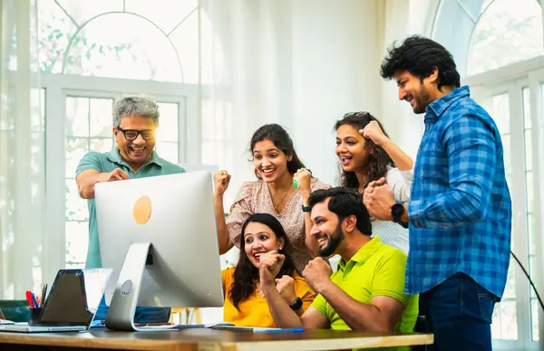 Hintli Asyalı genç iş adamları ya da teknoloji ortakları bilgisayarda çalışıyor, birden başarıyı beşlik çakarak kutluyorlar, modern rahat ofiste dizüstü bilgisayarla masada oturuyorlar.