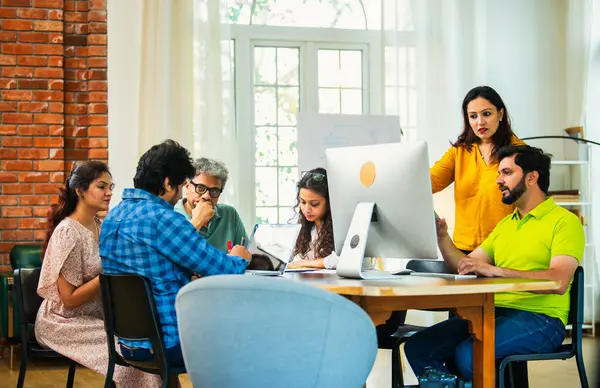 Hintli Asyalı genç iş adamları proje stratejisi üzerinde çalışan, belgeleri analiz eden, dizüstü bilgisayarda çalışan, iş geliştirme başarısı için samimi modern ofiste beyin fırtınası yapan bir ekip kurdular.
