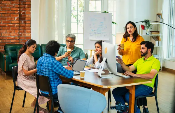 Hintli Asyalı genç iş adamları proje stratejisi üzerinde çalışan, belgeleri analiz eden, dizüstü bilgisayarda çalışan, iş geliştirme başarısı için samimi modern ofiste beyin fırtınası yapan bir ekip kurdular.