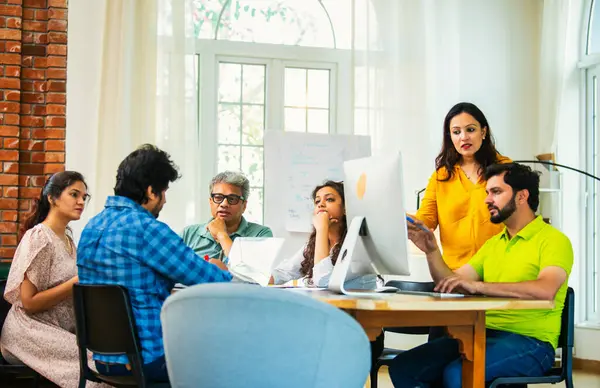 Hintli Asyalı genç iş adamları proje stratejisi üzerinde çalışan, belgeleri analiz eden, dizüstü bilgisayarda çalışan, iş geliştirme başarısı için samimi modern ofiste beyin fırtınası yapan bir ekip kurdular.