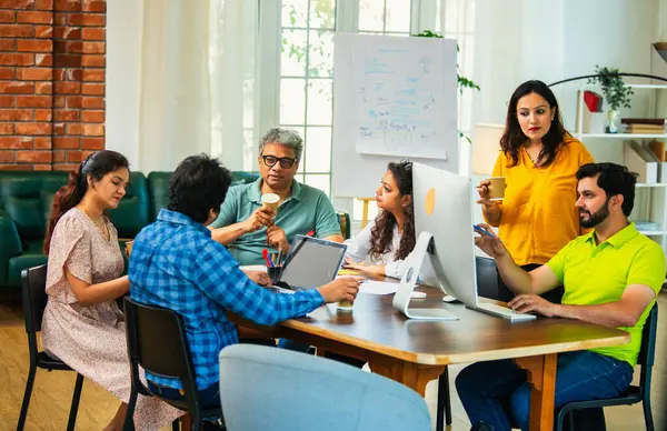 Hintli Asyalı genç iş adamları proje stratejisi üzerinde çalışan, belgeleri analiz eden, dizüstü bilgisayarda çalışan, iş geliştirme başarısı için samimi modern ofiste beyin fırtınası yapan bir ekip kurdular.