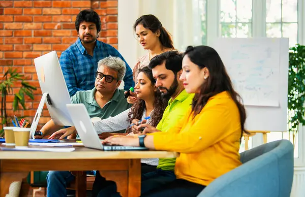 Hintli Asyalı genç iş adamları veya girişim ortakları önemli bir projede işbirliği yapıyor, bilgisayarda yoğun bir şekilde çalışıyor, tartışmalara katılan her takım üyesi, karar verme mekanizması