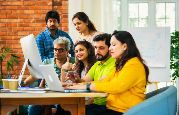 Hintli Asyalı genç iş adamları ya da teknoloji firması ortakları bilgisayarda çalışıyor, birden başarıyı beşlik çakarak kutluyorlar, modern rahat ofiste masa başında oturuyorlar.