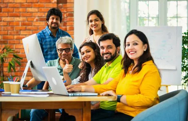 Hintli Asyalı genç iş adamları ya da teknoloji firması ortakları bilgisayarda çalışıyor, birden başarıyı beşlik çakarak kutluyorlar, modern rahat ofiste masa başında oturuyorlar.