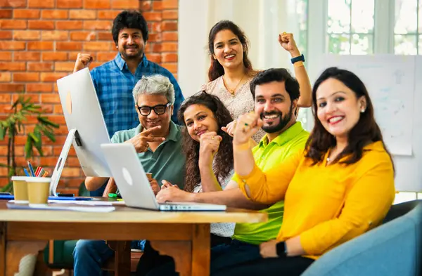 Hintli Asyalı genç iş adamları ya da teknoloji firması ortakları bilgisayarda çalışıyor, birden başarıyı beşlik çakarak kutluyorlar, modern rahat ofiste masa başında oturuyorlar.