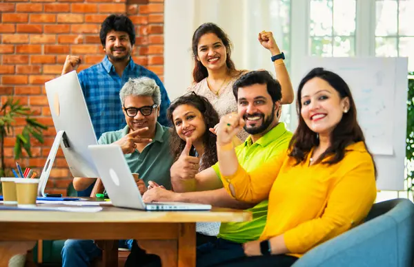 Hintli Asyalı genç iş adamları ya da teknoloji firması ortakları bilgisayarda çalışıyor, birden başarıyı beşlik çakarak kutluyorlar, modern rahat ofiste masa başında oturuyorlar.