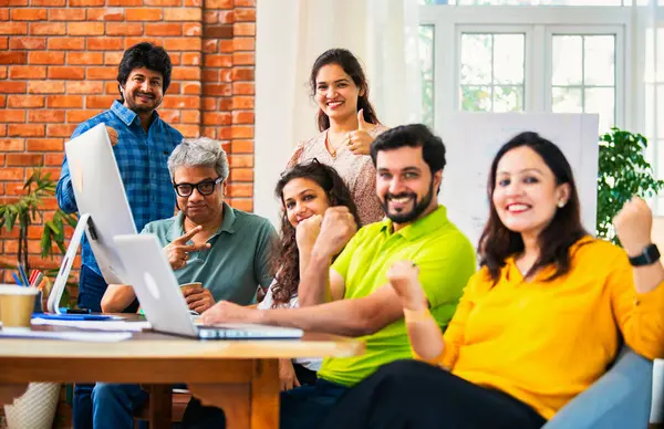 Hintli Asyalı genç iş adamları ya da teknoloji firması ortakları bilgisayarda çalışıyor, birden başarıyı beşlik çakarak kutluyorlar, modern rahat ofiste masa başında oturuyorlar.