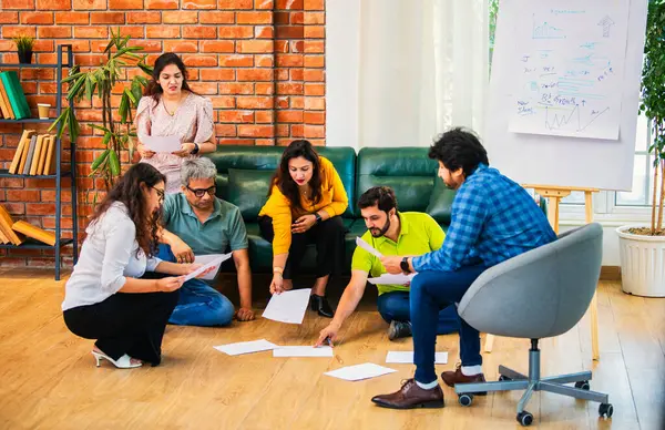 Hindistanlı Asyalı genç iş ortakları yeni ortaklar belgelerle önemli projeler planlarken modern, samimi, katılımcı ve takım çalışması olan ofiste birlikte oturuyorlar.