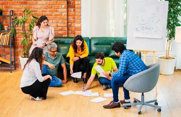 Hindistanlı Asyalı genç iş ortakları yeni ortaklar belgelerle önemli projeler planlarken modern, samimi, katılımcı ve takım çalışması olan ofiste birlikte oturuyorlar.