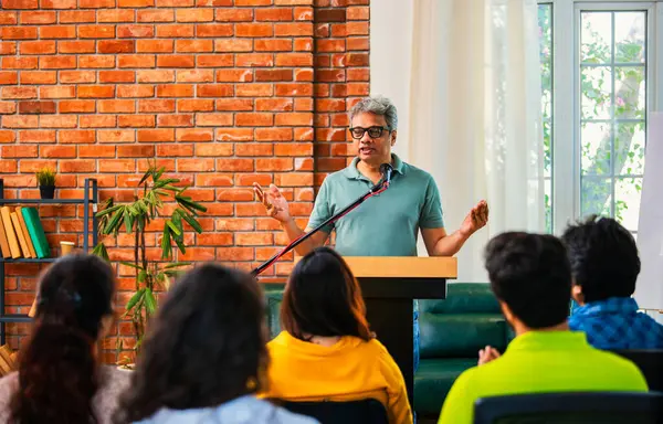 Hintli Asyalı yaşam koçu, profesyonel akıl hocası konferansta bir grup genç girişimciye iş büyümesi girişimciliği hakkında ilham verici bir konuşma yapıyor, mikrofonla podyumda güvenle konuşuyor.