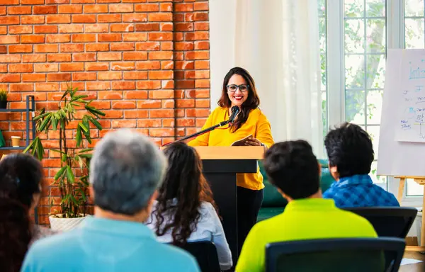 Hintli Asyalı yaşam koçu, profesyonel akıl hocası konferansta bir grup genç girişimciye iş büyümesi girişimciliği hakkında ilham verici bir konuşma yapıyor, mikrofonla podyumda güvenle konuşuyor.