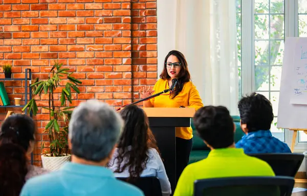 Hintli Asyalı yaşam koçu, profesyonel akıl hocası konferansta bir grup genç girişimciye iş büyümesi girişimciliği hakkında ilham verici bir konuşma yapıyor, mikrofonla podyumda güvenle konuşuyor.