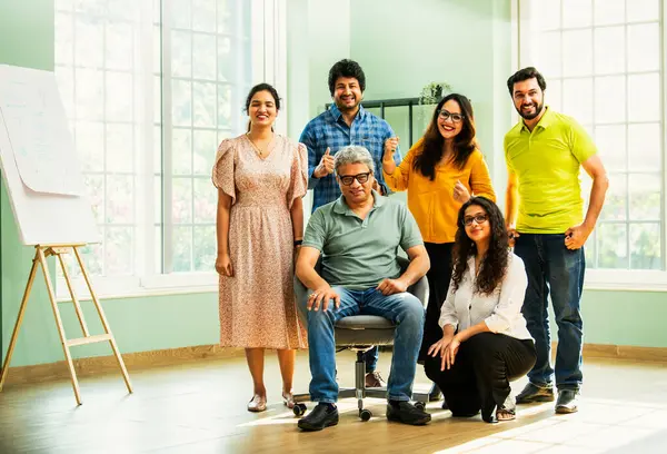 Genç girişimcilerden oluşan Hint Asya dinamik ekibi modern yaratıcı ofiste başarıyı kutluyor. Kameraya, takım çalışmasına, lidere gülümseyen iş adamlarına güveniyorlar.