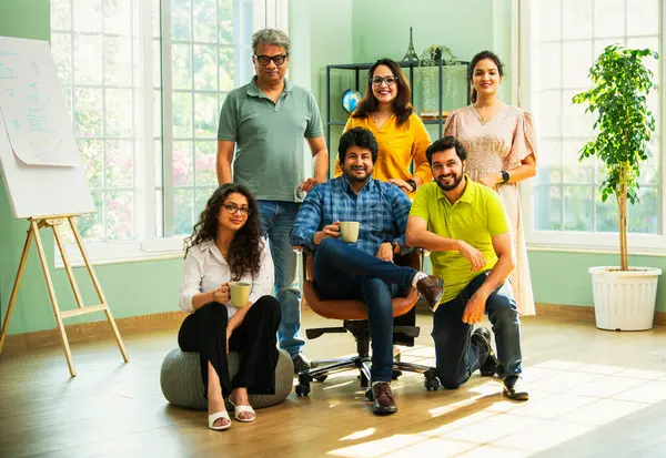 Genç girişimcilerden oluşan Hint Asya dinamik ekibi modern yaratıcı ofiste başarıyı kutluyor. Kameraya, takım çalışmasına, lidere gülümseyen iş adamlarına güveniyorlar.