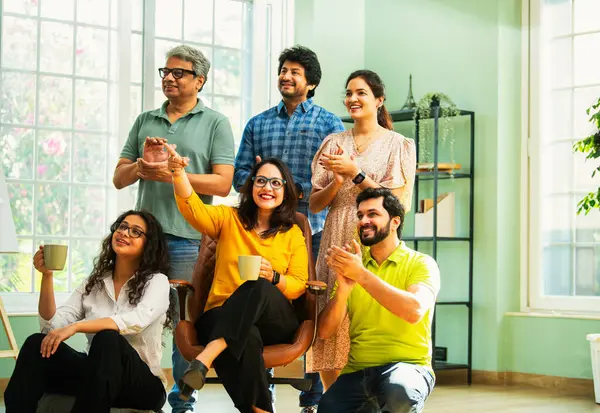 Modern girişim ofisindeki Hintli Asyalı genç şirket profesyonelleri, şık giyinmiş, el çırpıyor, başarıyı, başarıyı, takım çalışmasını, yeniliği, iş büyümesini kutluyorlar.