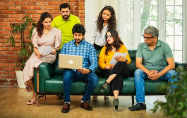 Hintli Asyalı genç girişimci, modern bir ofiste dizüstü bilgisayar ve belgelerle birlikte bir kanepede otururken fikir üretme ya da gayri resmi bir toplantıda strateji planlama ekibi kuruyor.