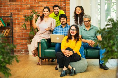 Hintli Asyalı genç girişimci, modern bir ofiste dizüstü bilgisayar ve belgelerle birlikte kanepede otururken gayri resmi bir toplantıda strateji planlarken başarıyı kutluyor.