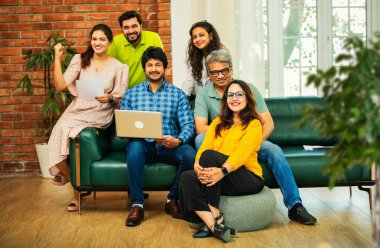 Hintli Asyalı genç girişimci, modern bir ofiste dizüstü bilgisayar ve belgelerle birlikte kanepede otururken gayri resmi bir toplantıda strateji planlarken başarıyı kutluyor.