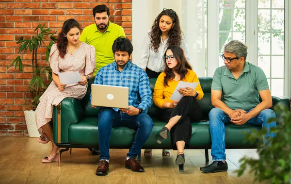 Hintli Asyalı genç girişimci, modern bir ofiste dizüstü bilgisayar ve belgelerle birlikte bir kanepede otururken fikir üretme ya da gayri resmi bir toplantıda strateji planlama ekibi kuruyor.