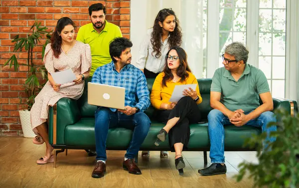 Hintli Asyalı genç girişimci, modern bir ofiste dizüstü bilgisayar ve belgelerle birlikte bir kanepede otururken fikir üretme ya da gayri resmi bir toplantıda strateji planlama ekibi kuruyor.