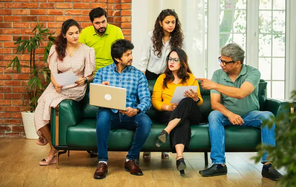 Hintli Asyalı genç girişimci, modern bir ofiste dizüstü bilgisayar ve belgelerle birlikte bir kanepede otururken fikir üretme ya da gayri resmi bir toplantıda strateji planlama ekibi kuruyor.