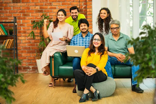 Hintli Asyalı genç girişimci, modern bir ofiste dizüstü bilgisayar ve belgelerle birlikte kanepede otururken gayri resmi bir toplantıda strateji planlarken başarıyı kutluyor.