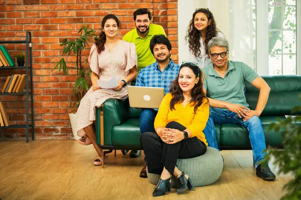 Hintli Asyalı genç girişimci, modern bir ofiste dizüstü bilgisayar ve belgelerle birlikte kanepede otururken gayri resmi bir toplantıda strateji planlarken başarıyı kutluyor.