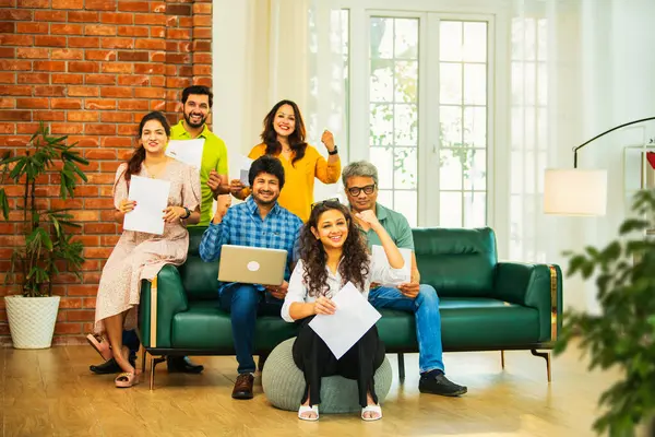 Hintli Asyalı genç girişimci, modern bir ofiste dizüstü bilgisayar ve belgelerle birlikte kanepede otururken gayri resmi bir toplantıda strateji planlarken başarıyı kutluyor.