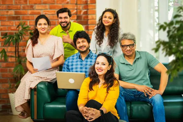 Hintli Asyalı genç girişimci, modern bir ofiste dizüstü bilgisayar ve belgelerle birlikte kanepede otururken gayri resmi bir toplantıda strateji planlarken başarıyı kutluyor.