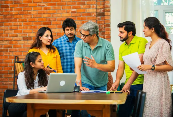 Hintli Asyalı genç iş adamları proje stratejisi üzerinde çalışan, belgeleri analiz eden, dizüstü bilgisayarda çalışan, iş geliştirme başarısı için samimi modern ofiste beyin fırtınası yapan bir ekip kurdular.