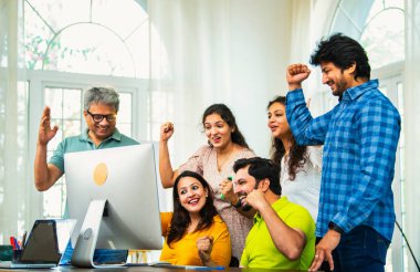Hintli Asyalı genç iş adamları ya da teknoloji ortakları bilgisayarda çalışıyor, birden başarıyı beşlik çakarak kutluyorlar, modern rahat ofiste dizüstü bilgisayarla masada oturuyorlar.