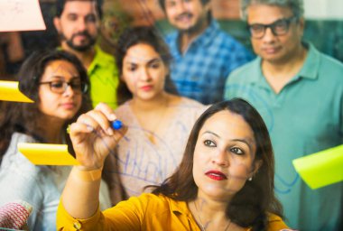 Hintli Asyalı genç iş adamları ya da yeni başlayan profesyonellerden oluşan bir grup. Fikir üreten, stratejileri tartışan, cam duvarın önünde kalem kullanarak projeler planlayan, modern ofisteki yapışkan notlar.